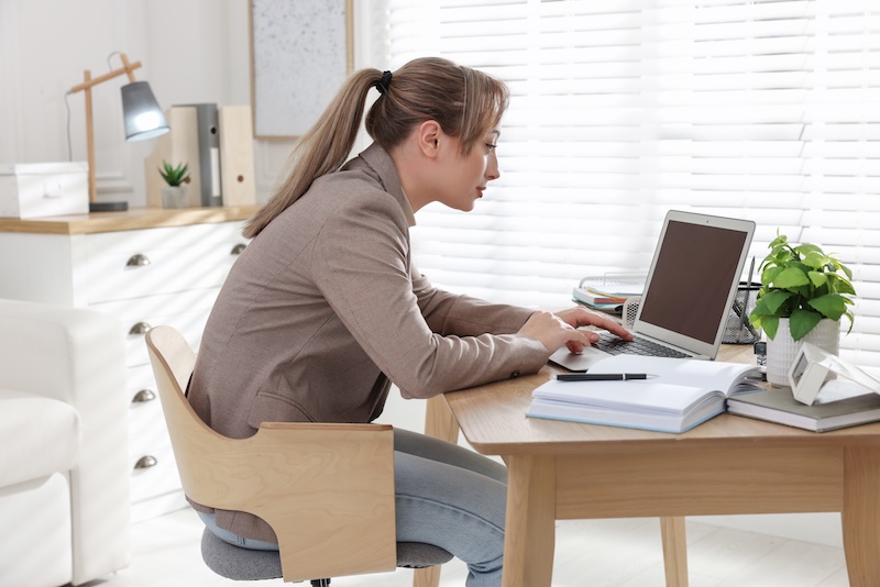 Young woman with poor posture using laptop at table indoors