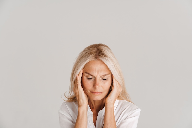Mature blonde woman with headache rubbing her temples isolated over white background