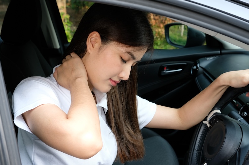 Beautiful young woman rubbing her neck, feeling sore after long drive. Female driver having terrible neck pain after whiplash injury in car crash. Healthcare, safety, pain concept